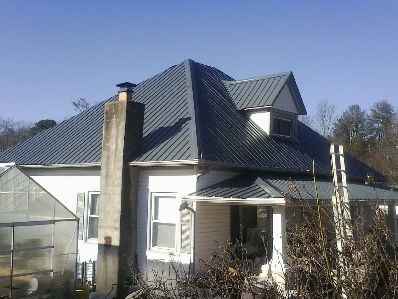 Dark blue standing seam metal roof on a white farmhouse with dormer — Slate & Tile Roof Repair by Roofing Brothers in Nesbit