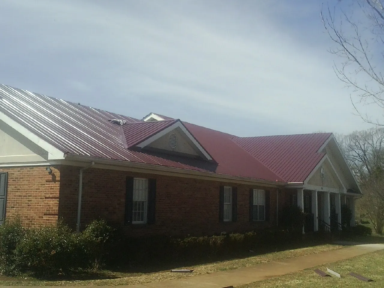 Red metal roof with gabled entries on a long brick building, from a Hail Damage Roof Repair job in Nesbit