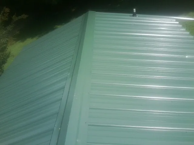 New green metal panels meeting at the ridge of a roof — Flat Roof Repair work by our crew in Nesbit