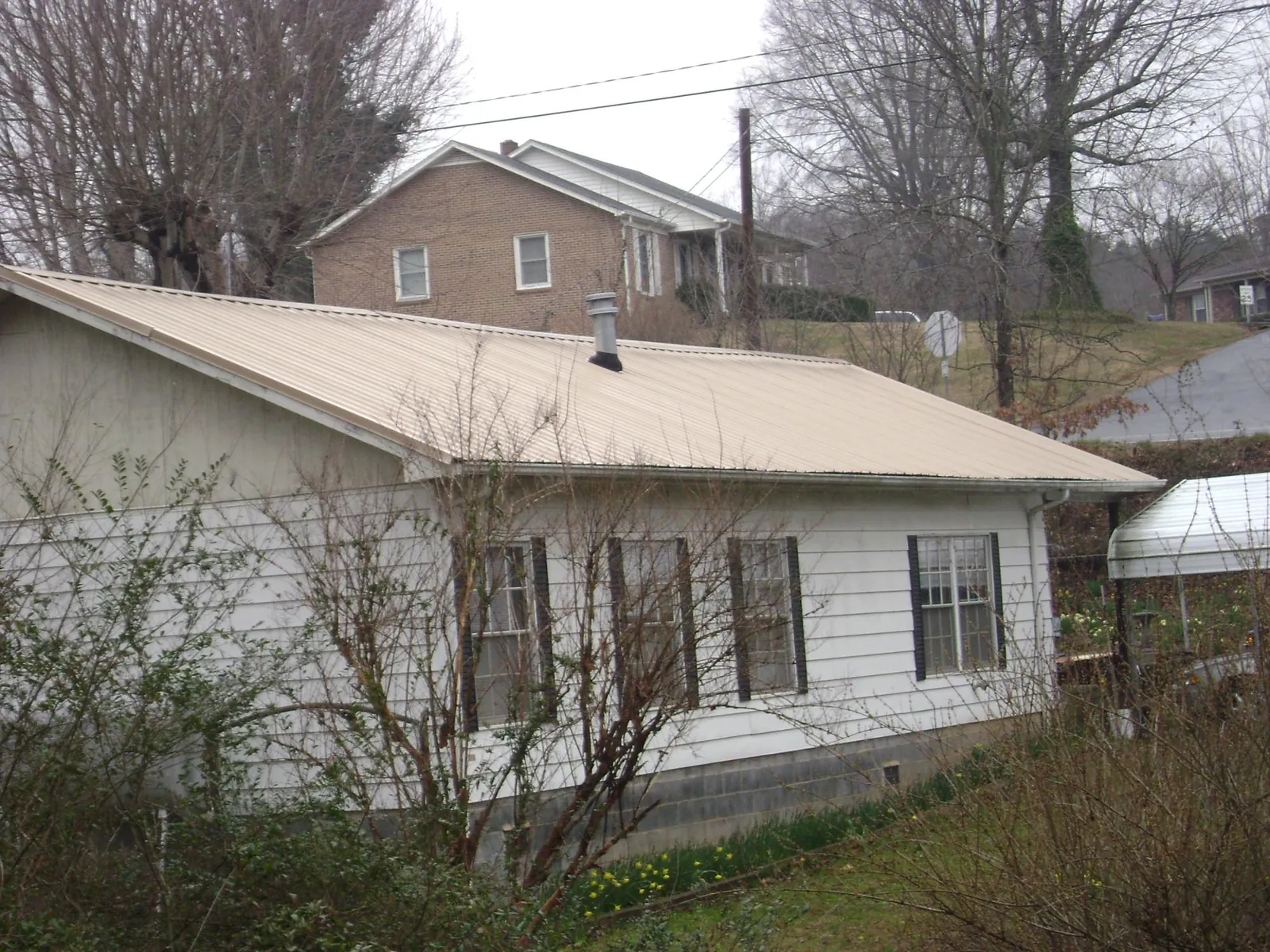 Tan metal roof on a white sided house set into a hillside — Commercial Roofing by Roofing Brothers in Nesbit